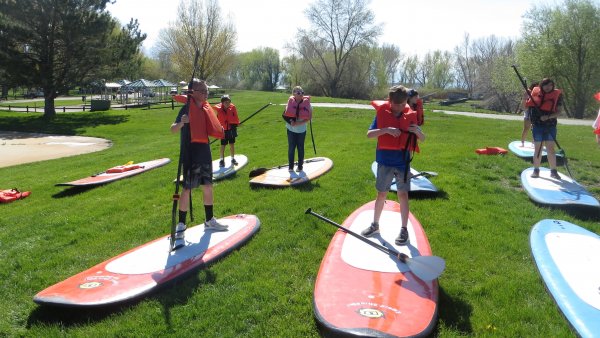 Kids standing on paddle-boards on the lawn.