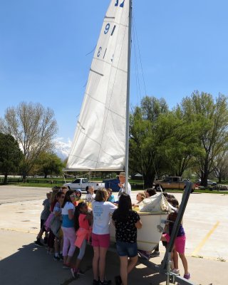 Kids standing around a sailboat.