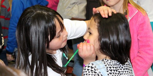 Young girl painting another child's face.