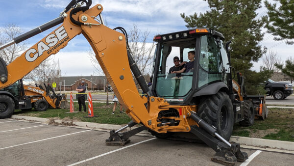 Student operating heavy equipment under direction of city employee.