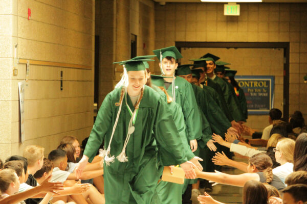 Graduates in caps and gowns greeting students as they progress around the school.