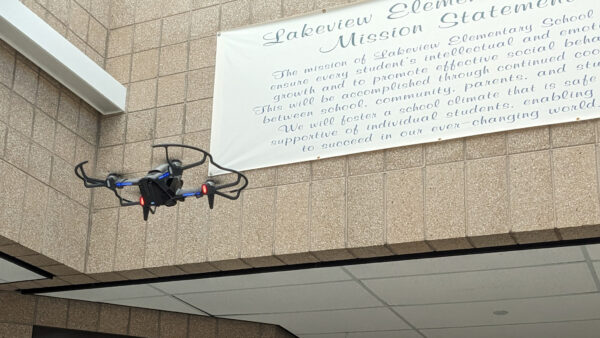 Drone flying by school motto sign.