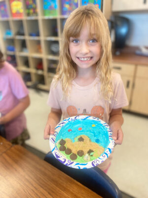 Girl with relief map created with icing and other edible treats on a paper plate.