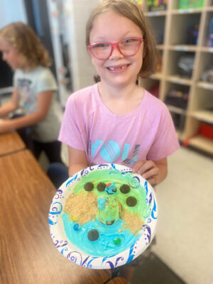Girl with relief map created with icing and other edible treats on a paper plate.