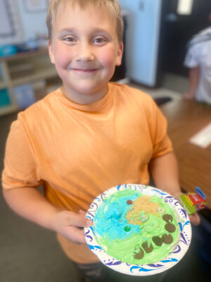 Boy with relief map created with icing and other edible treats on a paper plate.