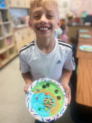 Young boy with relief map created with icing and other edible treats on a paper plate.