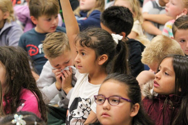 Young girl raises her hand in a crowd of students.