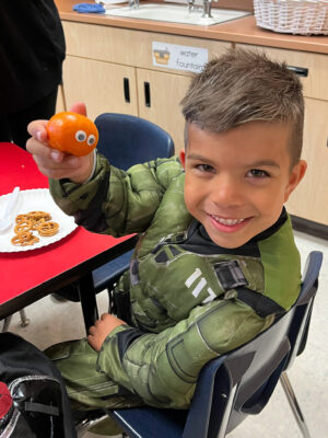 Young boy shows off his orange with googly eyes.
