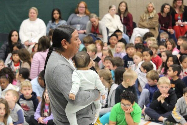 Man holding an infant speaks with students.