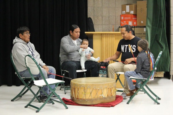 Three men waiting to play traditional drum in the company of their children.