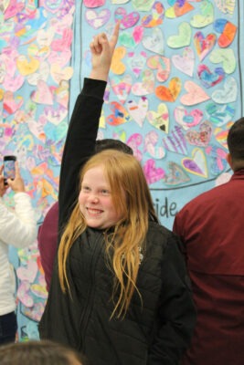 Young girl smiles as she points out her artwork.