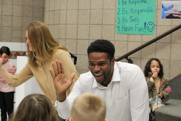 Man awaits a high-five from a young student.