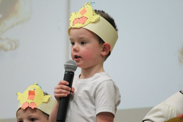 Kindergarten boy with chick headband speaking in microphone.