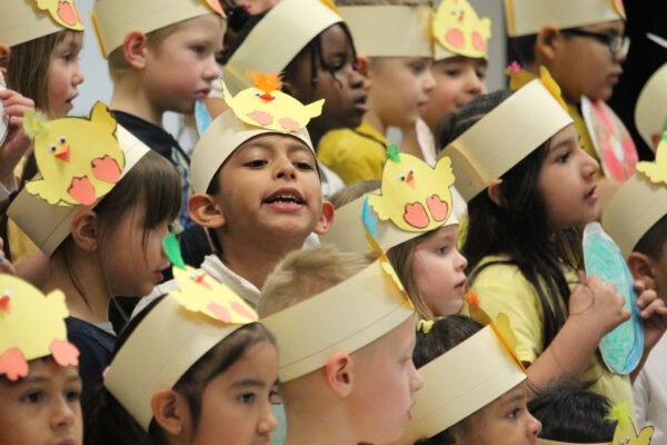 Kindergarten children, dressed in yellow and white, singing.